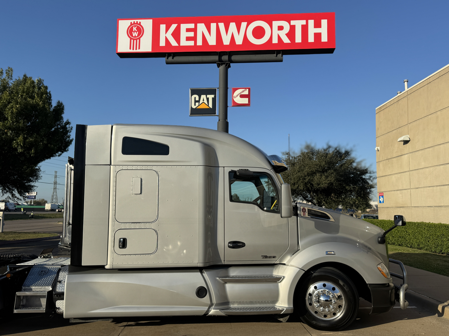 Kenworth truck cab and sleeper in front of a Kenworth sign, 2021 Kenworth T680 with silver color and chrome wheels.
