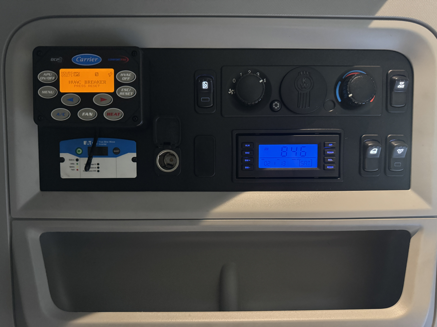 Kenworth dashboard panel showing control buttons, gauges, and digital display with blue backlight.