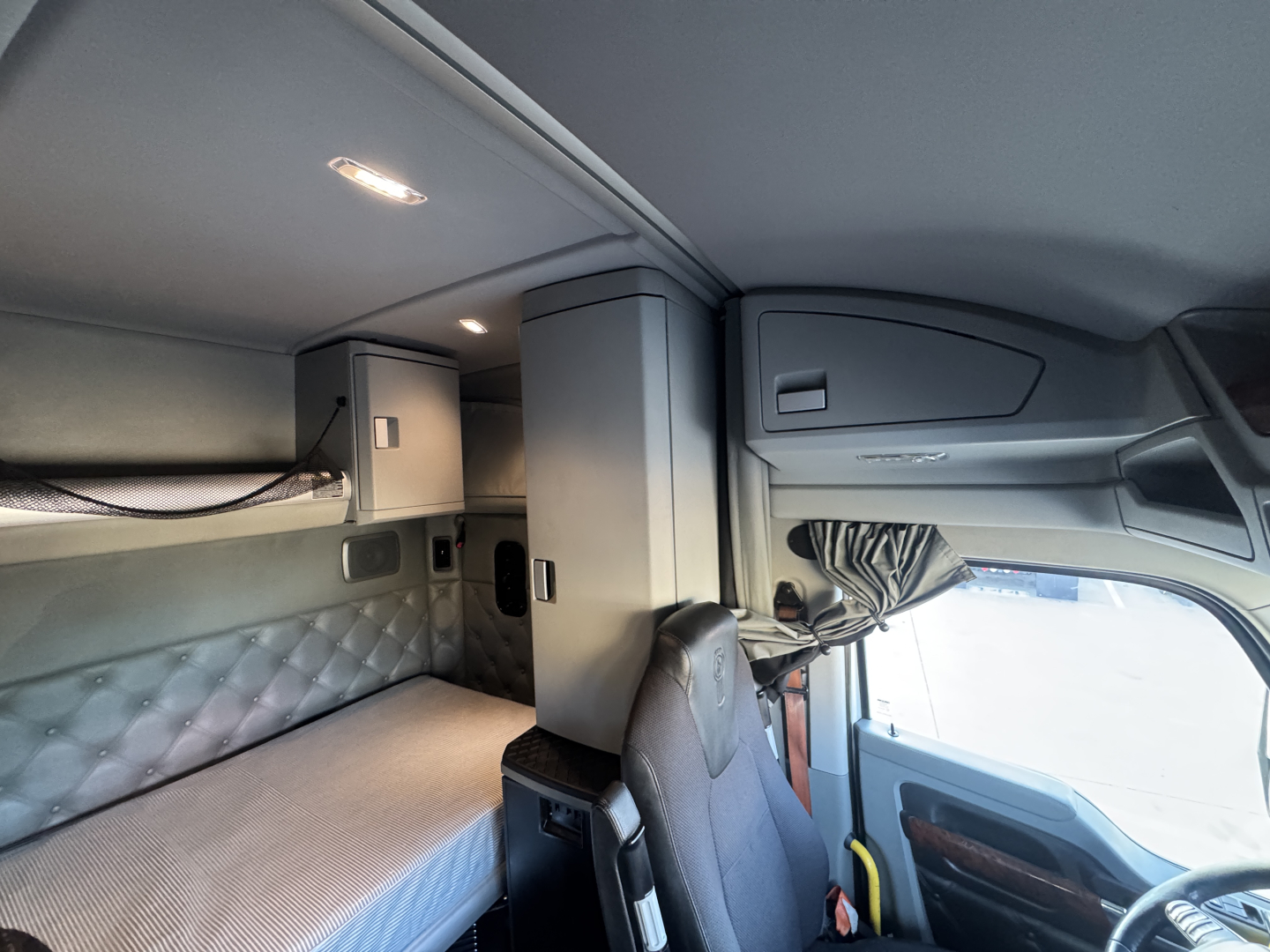 Kenworth T680 sleeper cab interior showing cockpit with dashboard and upper storage cabinet, driver seat, and bunk area in a used truck.