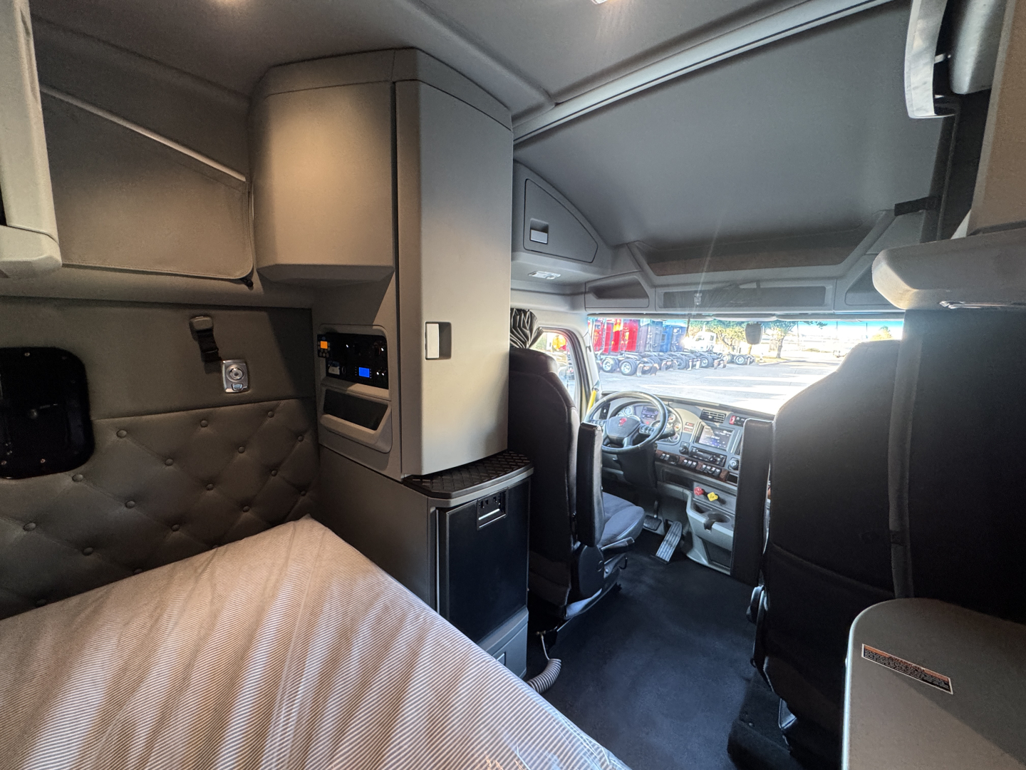 Interior of 2021 Kenworth T680 sleeper cab showing dashboard and driver seat area with overhead storage and partitions.