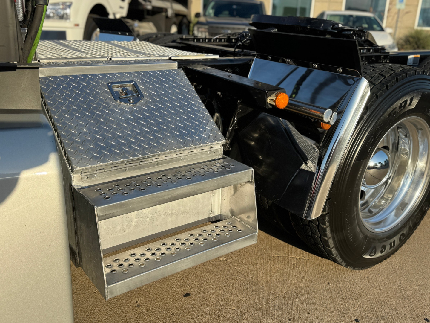 Kenworth truck rear/side step area with diamond plate toolbox, metal steps, and rear wheel visible.
