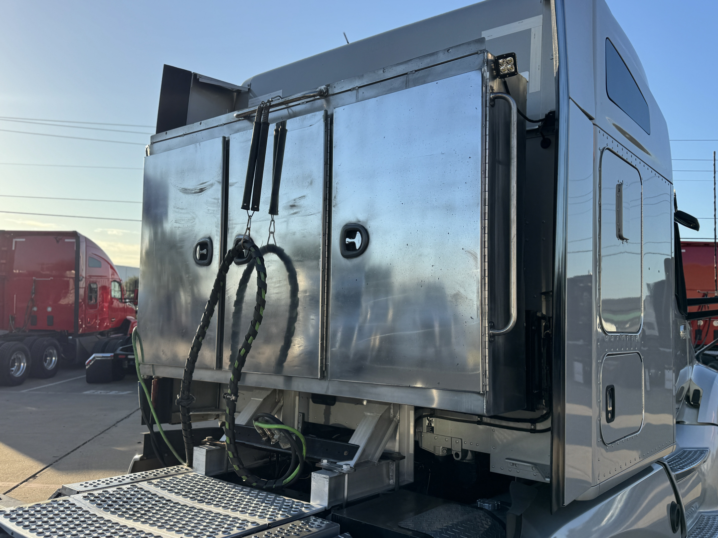 Kenworth T680 truck sleeper cab rear with polished aluminum storage boxes and hoses, side view showing cargo area and rear access door.