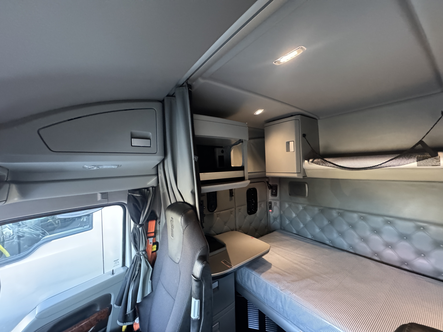 Kenworth T680 sleeper cab interior showing upper bunk area, overhead cabinets, and control panels.