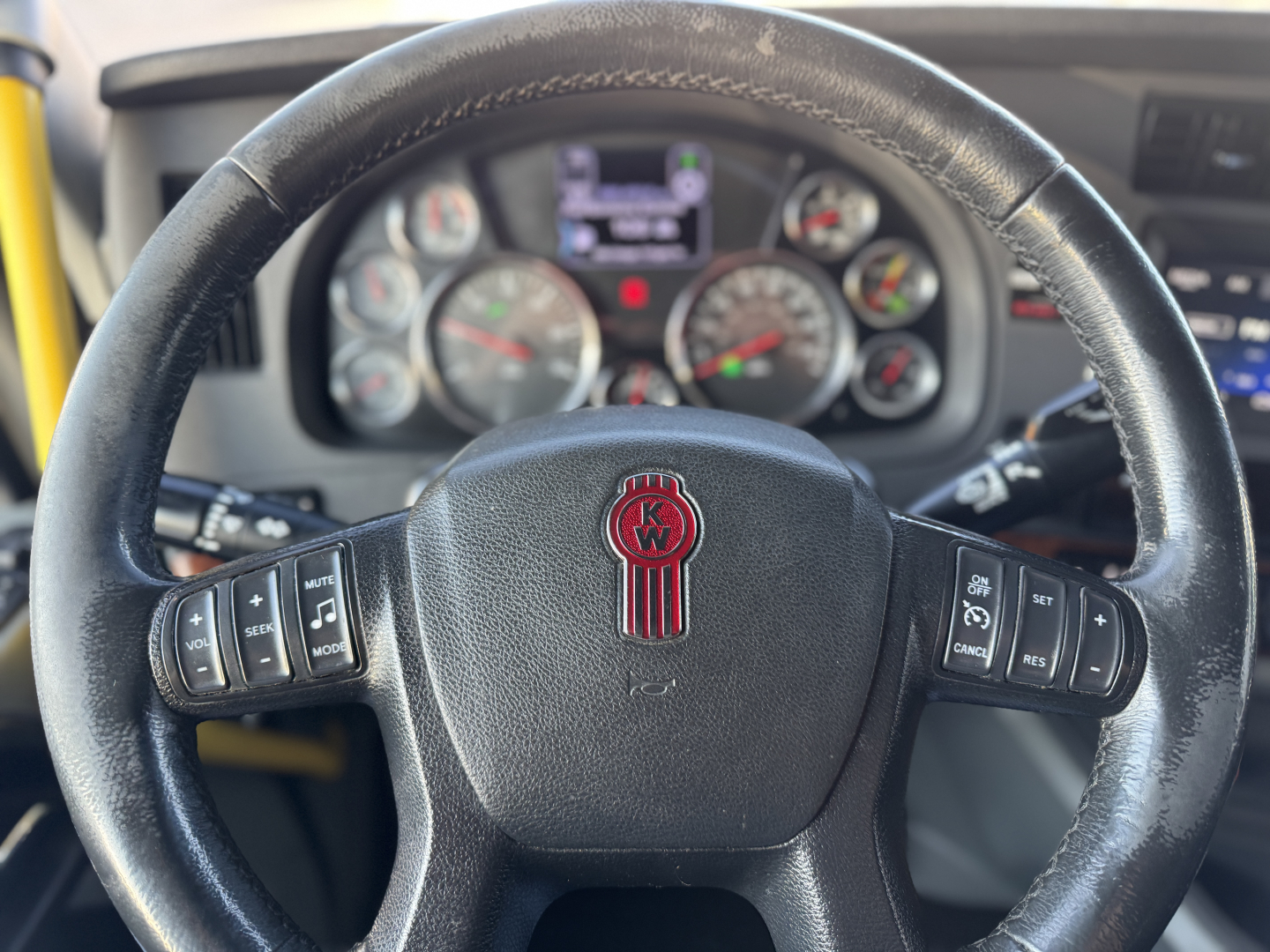 Kenworth T680 steering wheel with instrument cluster in the background; visible KW emblem on the steering wheel center.