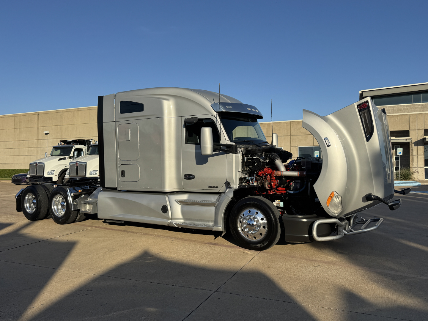 Kenworth T680 tractor with hood open, showing engine and side view. Front fender, chrome wheels, and gray body. No visible text labels.