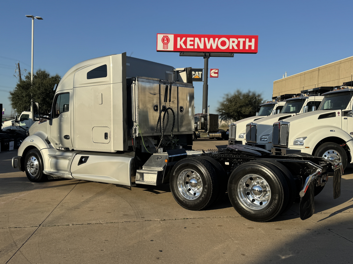 Kenworth T680 tractor in a dealership lot, side view showing sleeper cab and rear tandem with chrome wheels and black chassis.