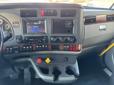 Kenworth T680 interior dashboard showing steering wheel, radio, climate controls, multiple switches, cup holders, and storage compartments.