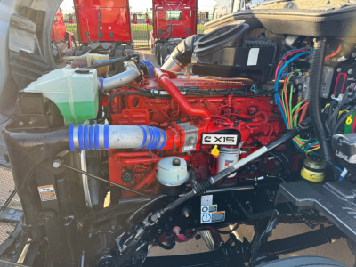 Kenworth T680 engine bay with red engine, blue silicone hose, green coolant reservoir, wiring looms, and various labeled components visible.