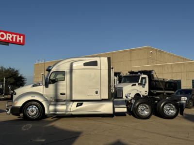 Kenworth T680 tractor-trailer in a dealership lot, side view with sleeper cab and dual rear axles.
