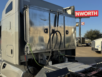 Kenworth T680 sleeper cab truck with a large steel utility body mounted behind the cab, dual ropes and hoses hanging, at a dealership lot.