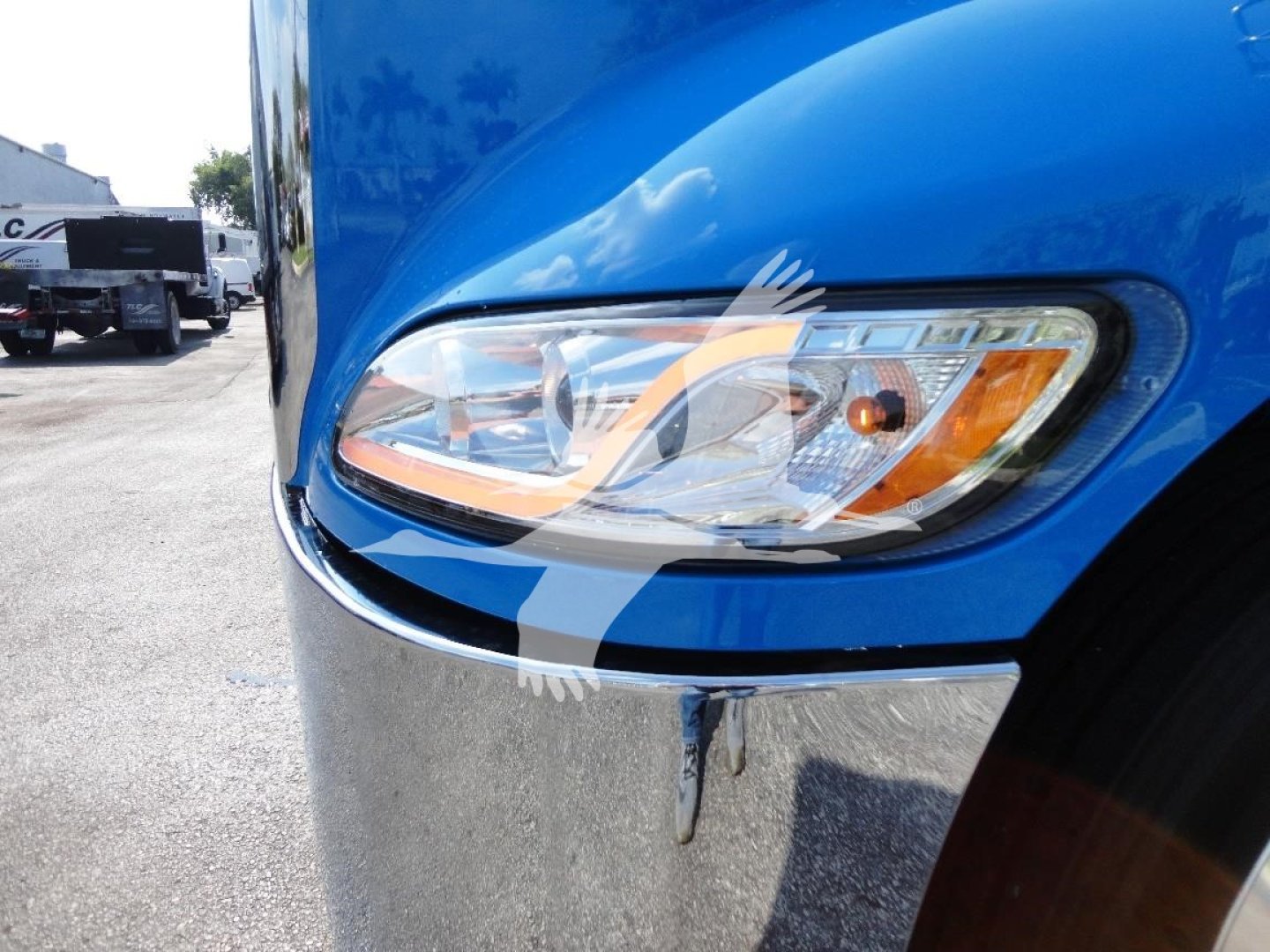 Headlight close-up on blue Peterbilt truck with chrome bumper and fender; front left area visible.