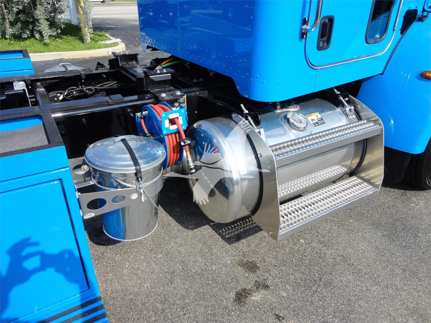 Peterbilt 337 fuel tank area with chrome cylindrical tank and steps, blue truck cab side showing undercarriage components.