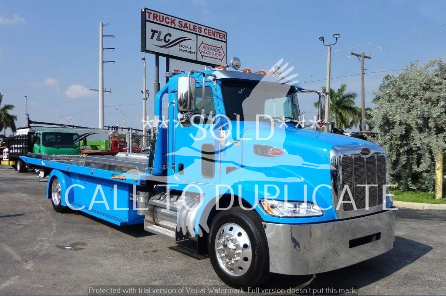 Peterbilt 337 rollback tow truck in blue, front-right view with flatbed and chrome bumper, stock# J56606, TLC logo signage in background.