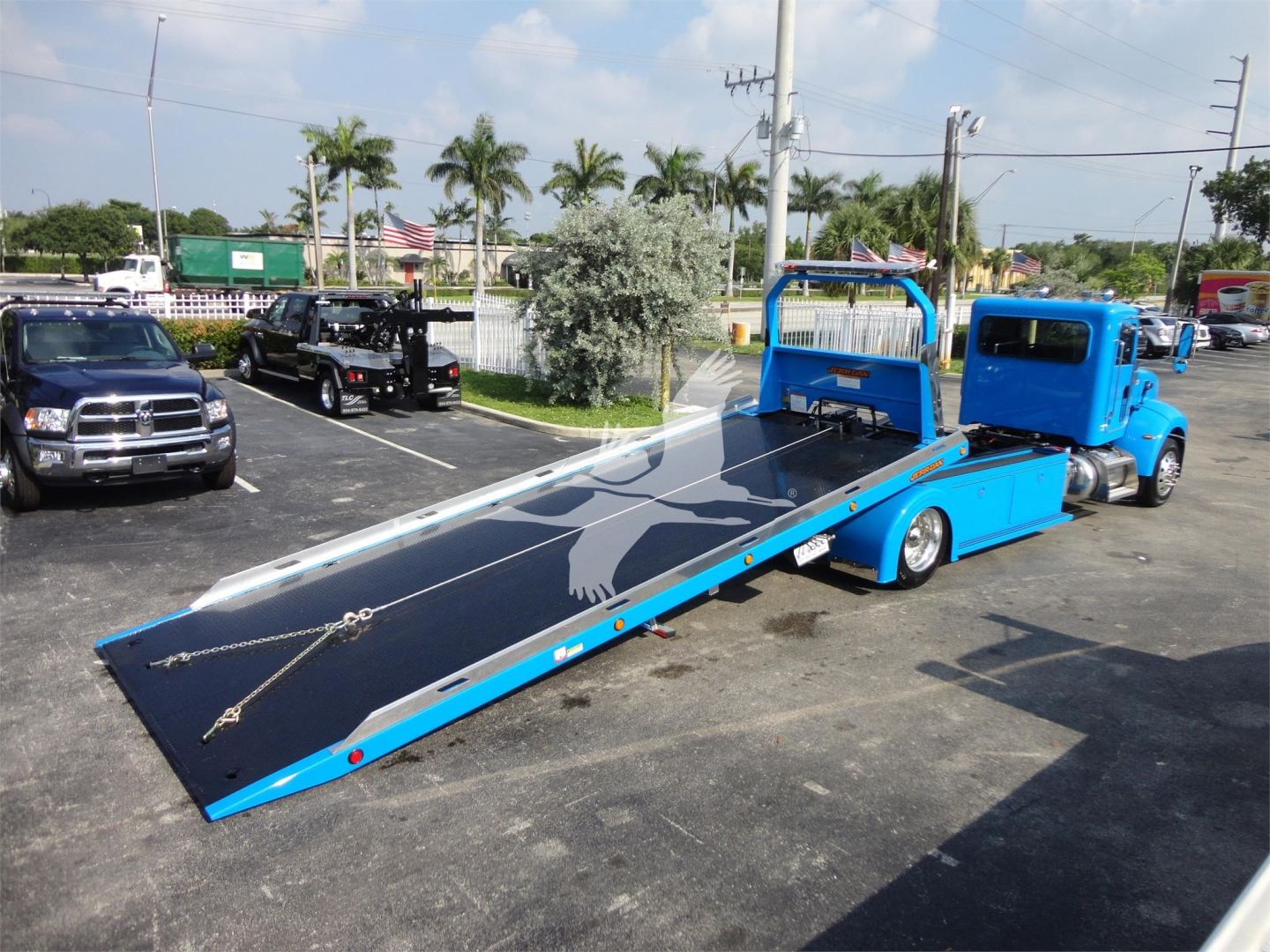 Peterbilt 337 rollback truck with a lowered blue hydraulic tow bed and black deck, stock number J56606, blue cab, white eagle decal on bed, showroom lot in background.