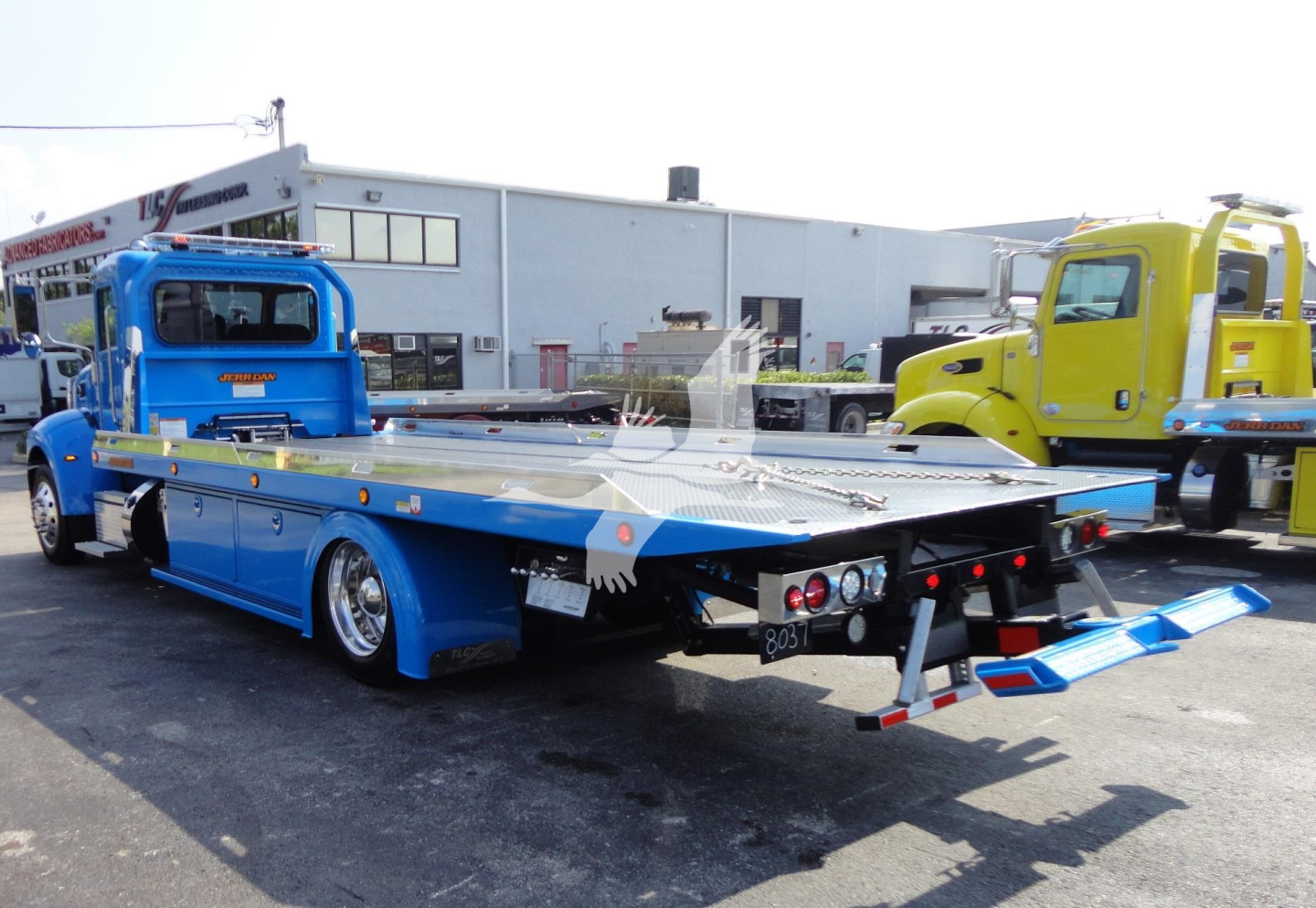 Peterbilt 337 rollback truck with blue cab, flatbed, and rear loading ramps.
