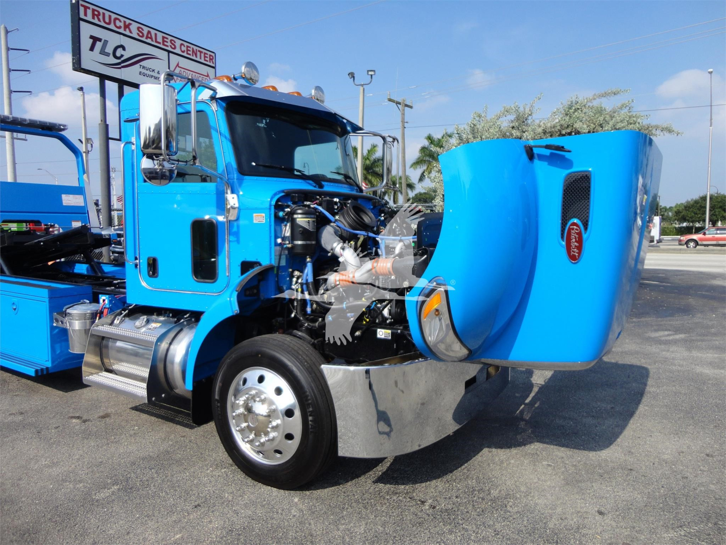 Peterbilt 337 rollback truck with raised blue hood showing engine and chrome wheel, blue cab, daytime dealership lot