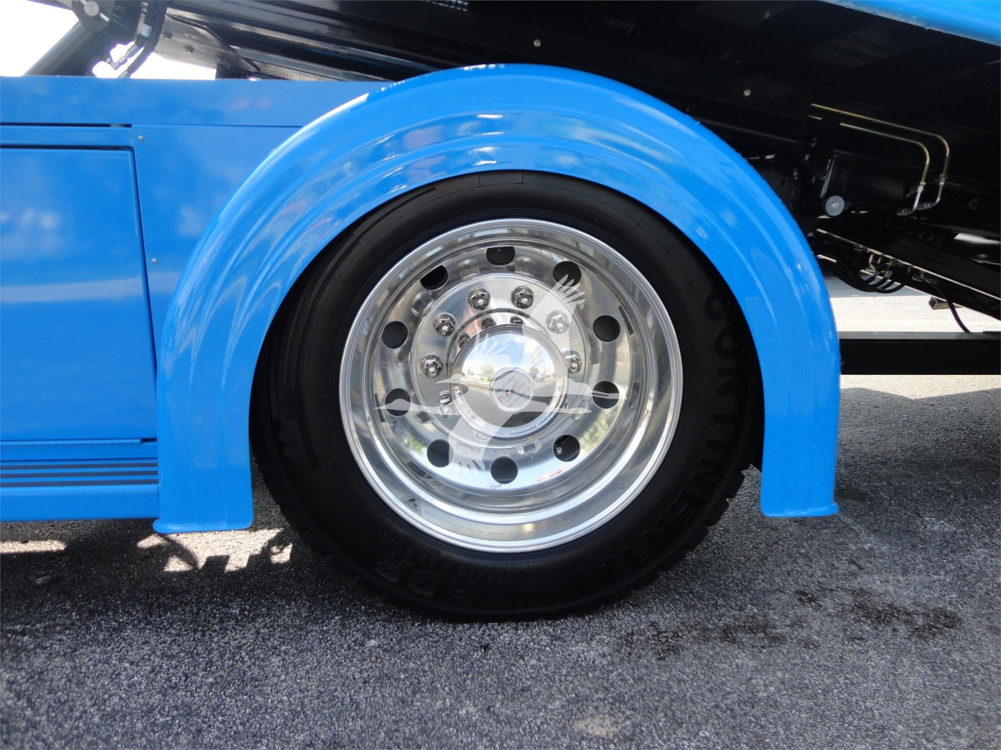 Truck wheel and fender close-up showing polished aluminum rim, blue fender, and black tire with visible lug nut holes.