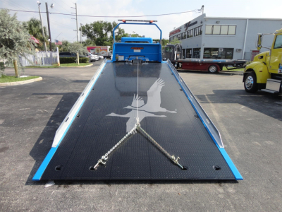 Truck bed on a 2022 Peterbilt 337 rollback with a black diamond plate ramp and blue frame, loading chains at the front, and a white bird logo on the ramp.