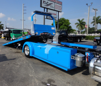 Blue Peterbilt 337 rollback tow truck side view showing mid-ship flatbed with hydraulic mechanism and chrome exhaust components.