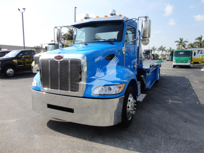 Blue Peterbilt 337 rollback truck viewed from front-right, chrome grille, large bumper, side steps, and cargo bed area visible.