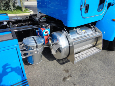 Peterbilt 337 fuel tank area with chrome cylindrical tank and steps, blue truck cab side showing undercarriage components.
