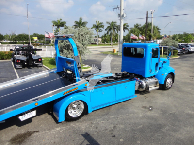 Peterbilt 337 rollback truck with bright blue cab and rollback bed, side view showing low-profile wheel, hydraulic winch, and chrome accents.