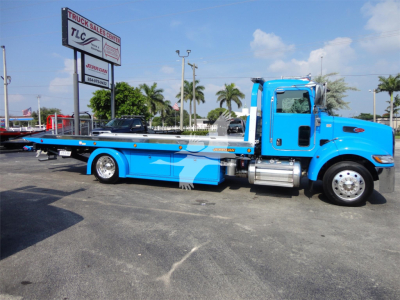 Peterbilt 337 tow truck in bright blue with a long rollback bed, cab-forward design, chrome fuel tanks, and side steps visible