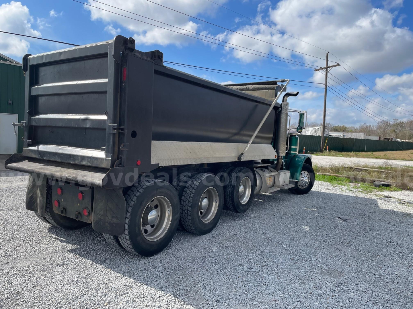 2009 Peterbilt 388 dump truck with black dump bed, green cab, three rear axles, parked on gravel. Visible text on truck/dump: none clearly legible; no serials or labels readable.