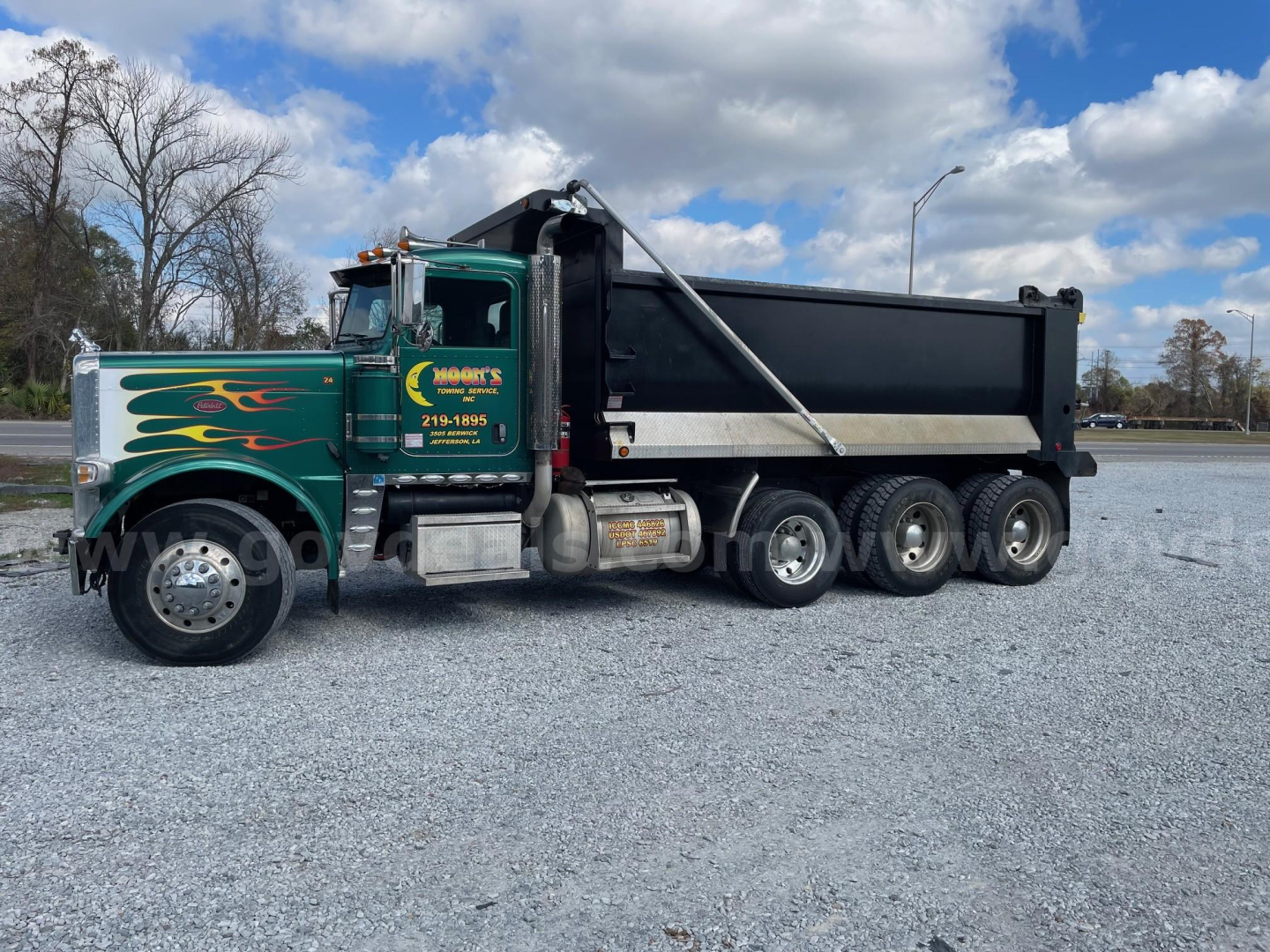 Peterbilt 388 dump truck in green with flame decals, side view showing dump bed and triple rear axles.