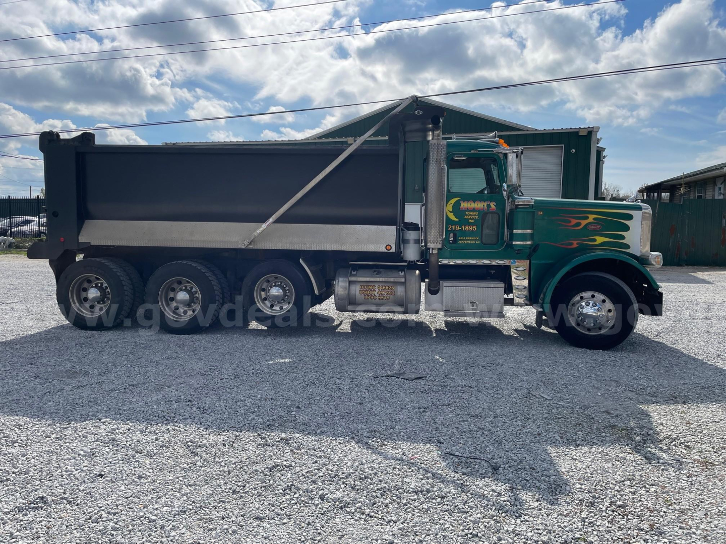 Peterbilt 388 dump truck side view showing green cab with flame graphics and a dark dump body.
