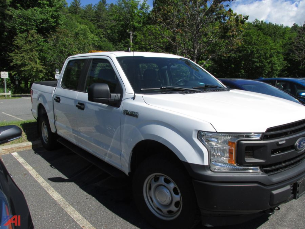 Ford F-150 Crew Cab pickup truck in a parking lot, white exterior, side view showing front grille and wheel wells.