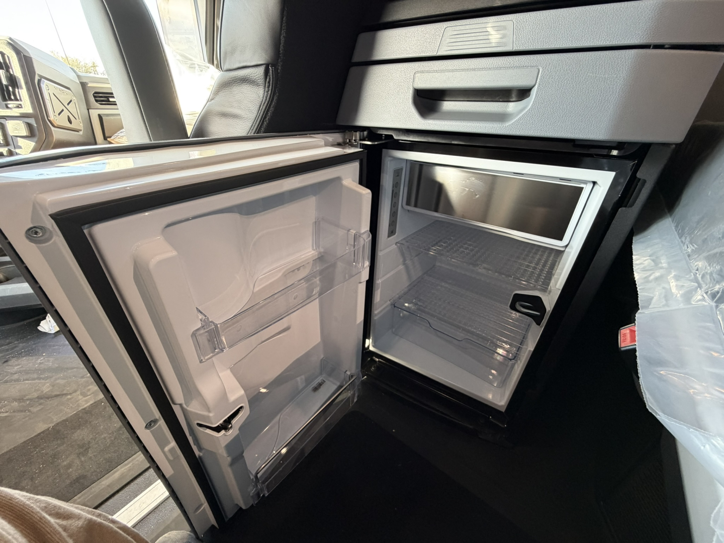 Fridge/freezer in truck cab shows compact under-counter fridge with empty freezer and shelves; interior light visible.