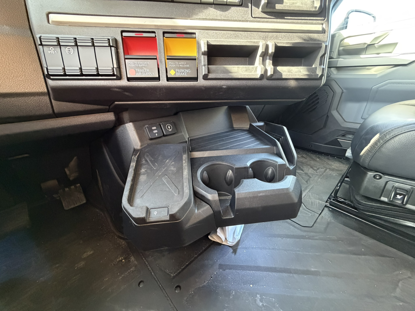 Mack PR64T76H interior showing lower dash with controls, cupholders, and switch panel near driver seat.
