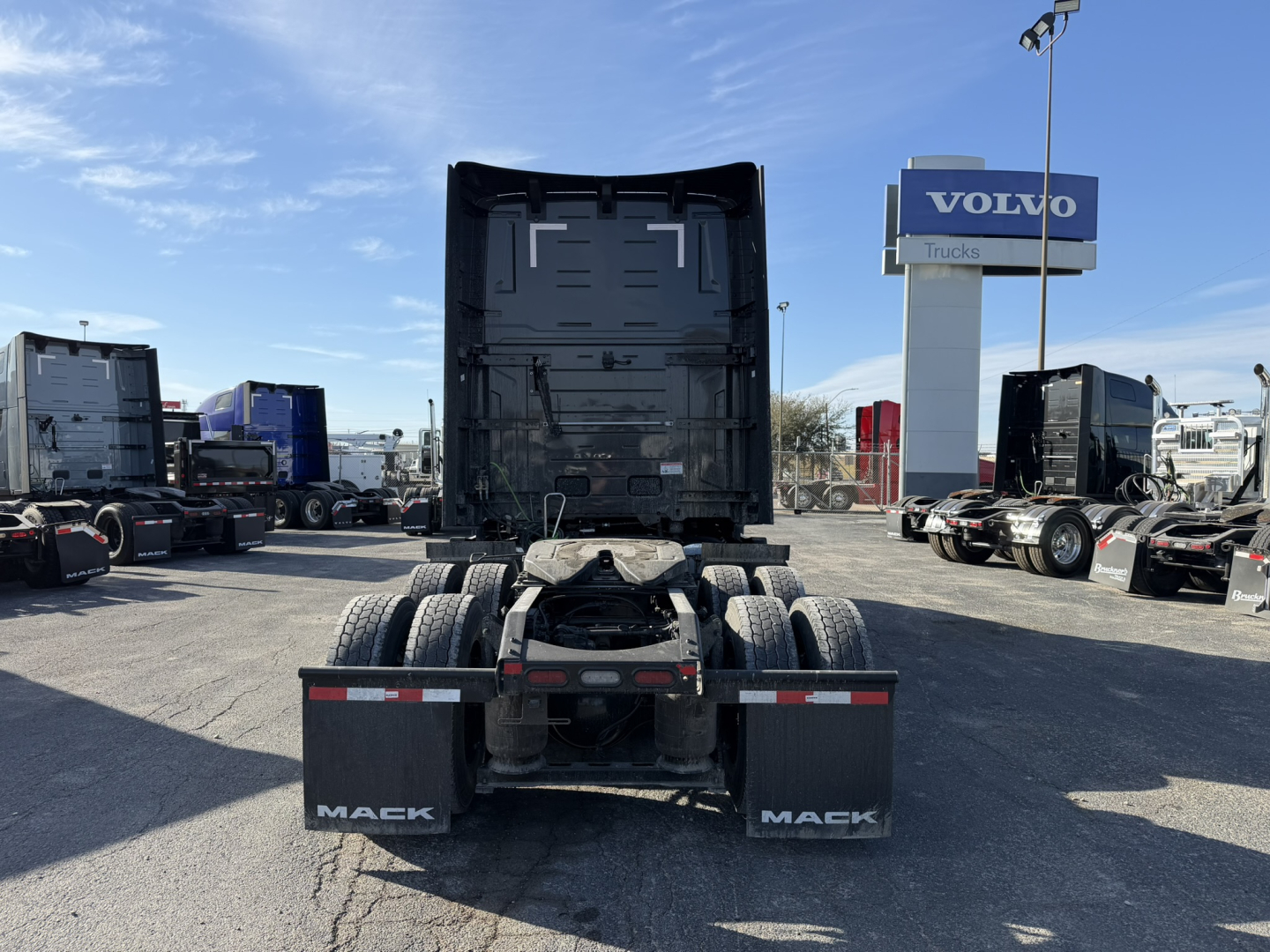 Mack PR64T76H truck tractor rear view showing fifth-wheel and dual rear axles, black sleeper cab area, and Mack mud flaps with white text. Serial/stock not visible.