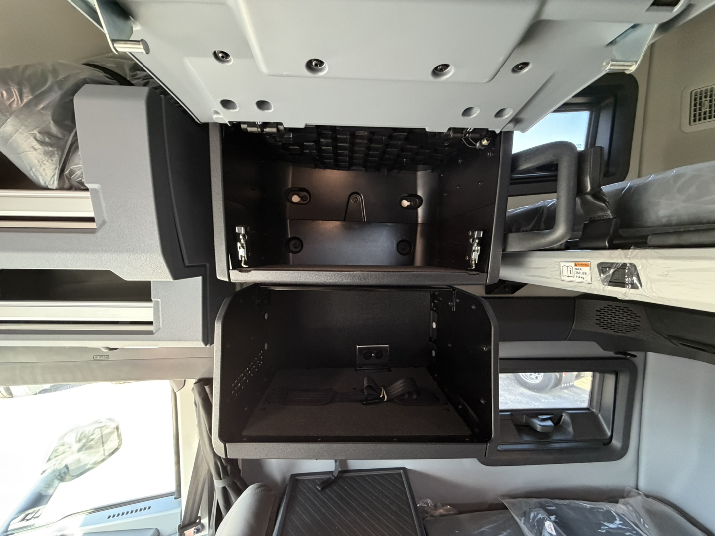 Cab interior of a Mack PR64T76H showing under-seat storage compartments with open compartments and metal framework.
