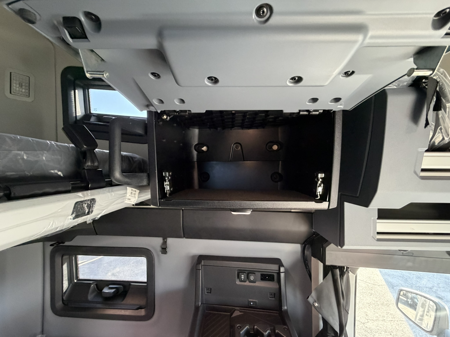 Mack PR64T76H cab interior showing empty upper storage compartment and dash area with controls and side window.