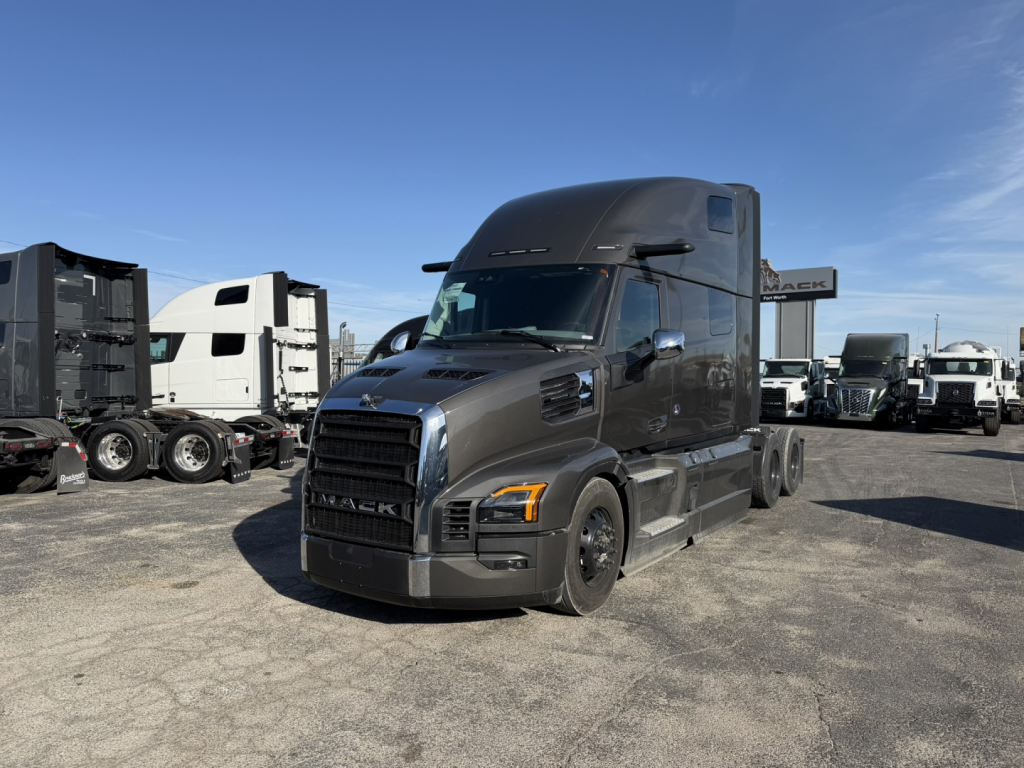 Mack PR64T76H conventional sleeper truck in a dealership lot, gray exterior, large cab, multiple trucks in background.