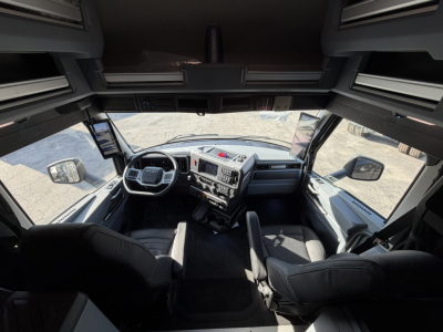 Truck cab interior of a 2026 Mack PR64T76H showing dashboard, steering wheel, and front seats from a wide-angle perspective.