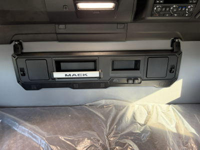 Truck interior upper dash area with Mack badge and center console panel showing two rectangular openings and storage compartment.