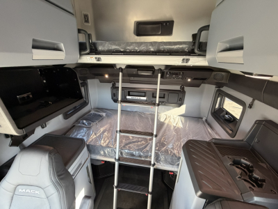 Mack PR64T76H sleeper cab interior showing upper bunk, cabinetry, and control panel with ladder and plastic-wrapped mattress.