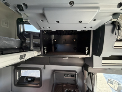 Mack PR64T76H cab interior showing empty upper storage compartment and dash area with controls and side window.
