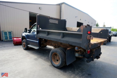 Ford F-350 XL SD dump bed truck with plow attachment in a yard, rear view showing dump bed and dual rear wheels