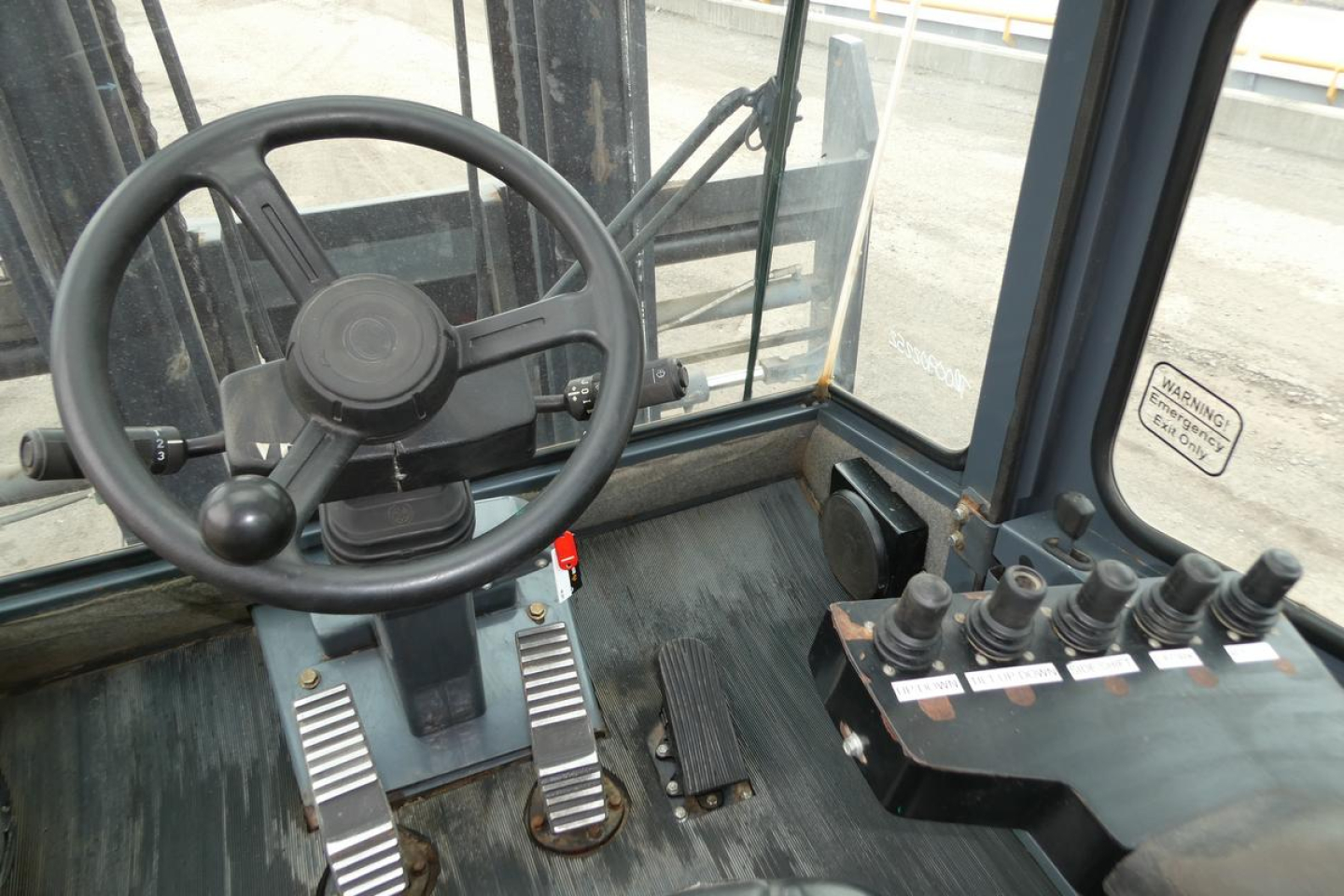 Operator cab of a forklift with steering wheel, two pedals, and a control lever panel on right side showing multiple levers and labels.
