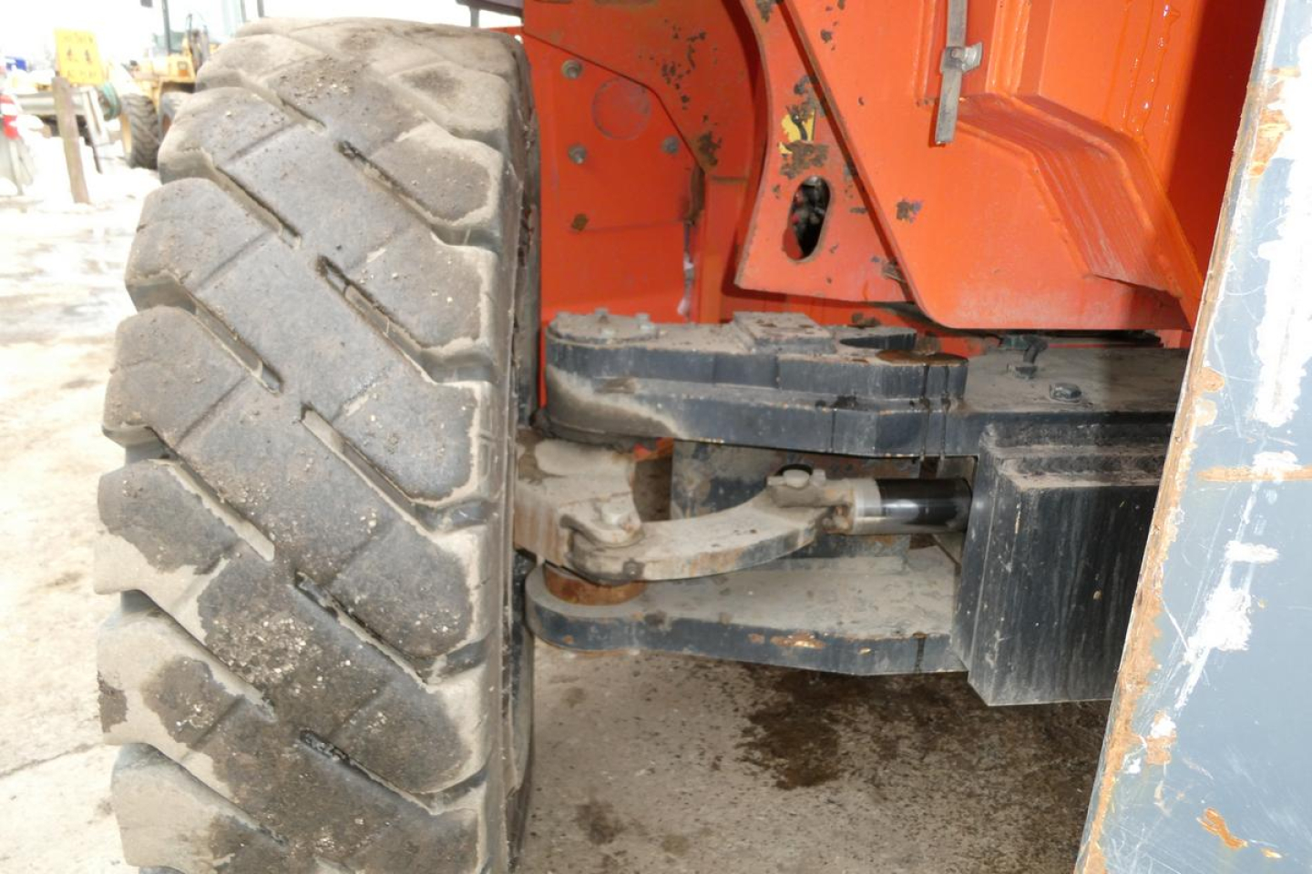 Truck/industrial lift showing large rugged tire, axle, and orange-painted frame with hydraulic components visible.