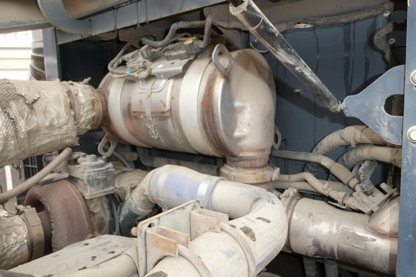 Engine bay showing hoses, turbocharger, exhaust pipe, and components of a heavy-duty truck lift system.
