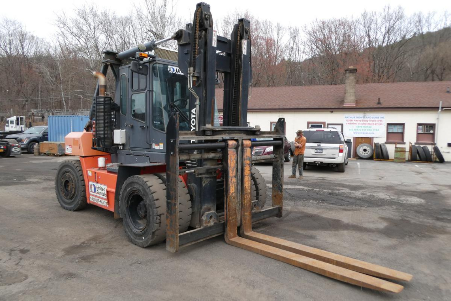 Truck-mounted forklift (Toyota THD3000-24) in use showing lifting arms and forks in yard.