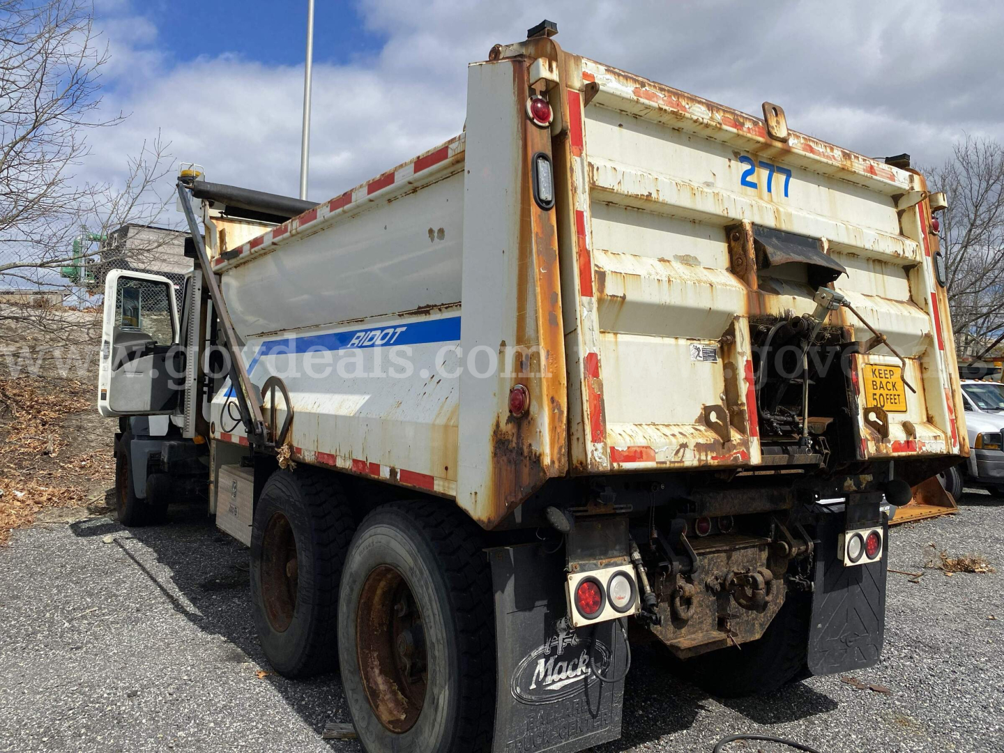 Dump truck rear view with dirty white MACK GU713 dump body, two rear axles, visible Arkansas-style back plate, and rusted edges.