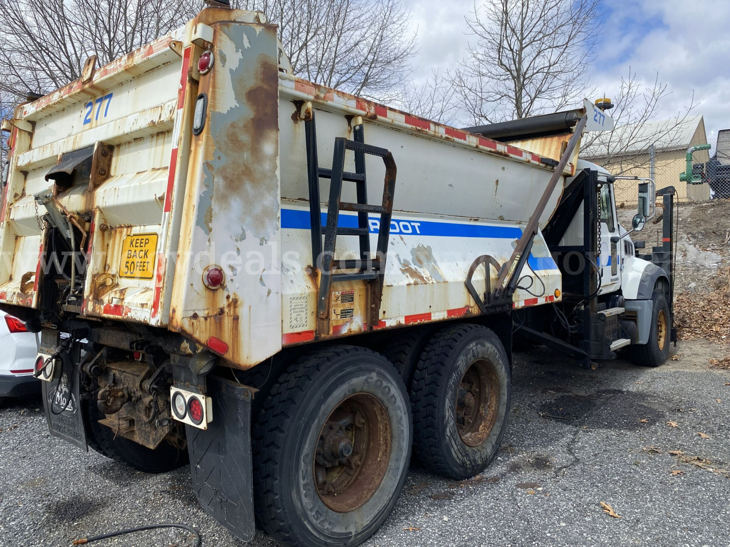 Dump truck rear and side view showing dump bed with rust and faded white paint, Mack GU713 with dual rear axles.