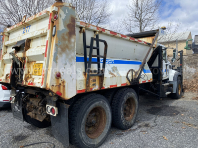 Dump truck rear and side view showing dump bed with rust and faded white paint, Mack GU713 with dual rear axles.