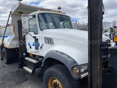 Mack GU713 dump truck with white cab, front view showing side steps and large fender, VIN plate not visible, heavy equipment in background.